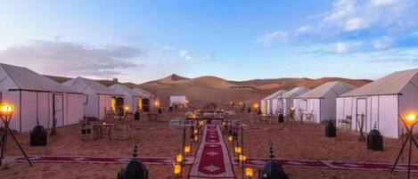 Un campamento en el desierto con tiendas dispuestas en filas, un pasillo central y faroles.