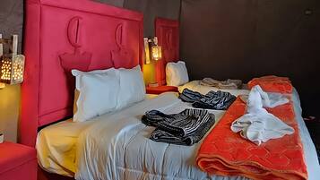 A modern hotel room with a sloped ceiling, a red headboard, a large bed with white and orange bedding, and a hanging light fixture.