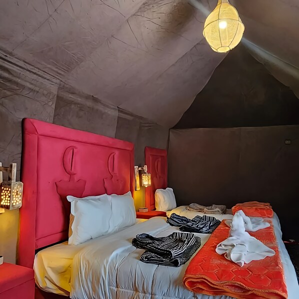 A modern hotel room with a sloped ceiling, a red headboard, a large bed with white and orange bedding, and a hanging light fixture.