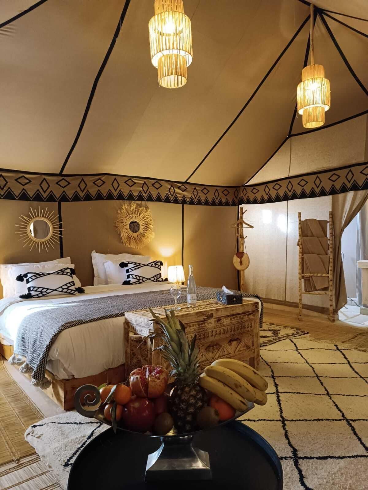 Ein Zeltraum mit Bett, hängenden Lampen und einer Obstschale auf dem Boden.