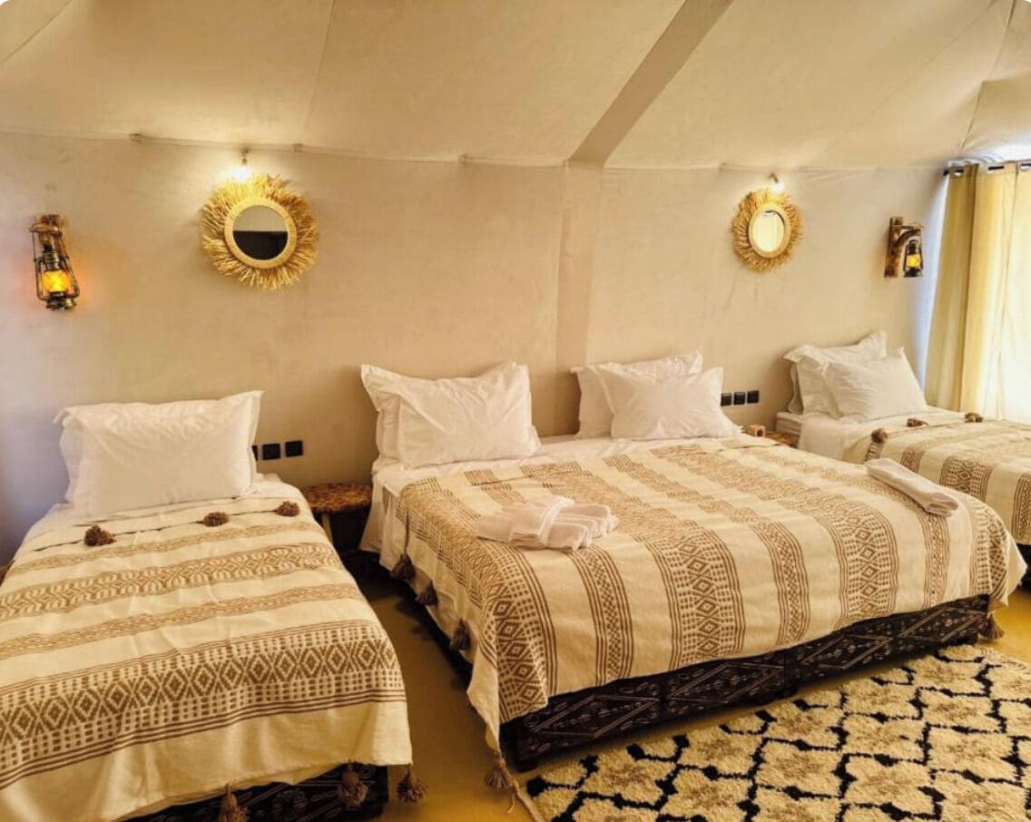 Een hotelkamer met drie bedden, elk voorzien van beddengoed met een patroon, een grote spiegel aan de muur en een vloerkleed.