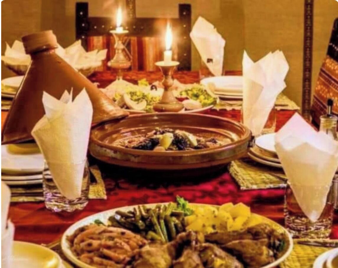 Una mesa de comedor servida con platos tradicionales marroquíes, un hervidor de té y una jarra de peltre.