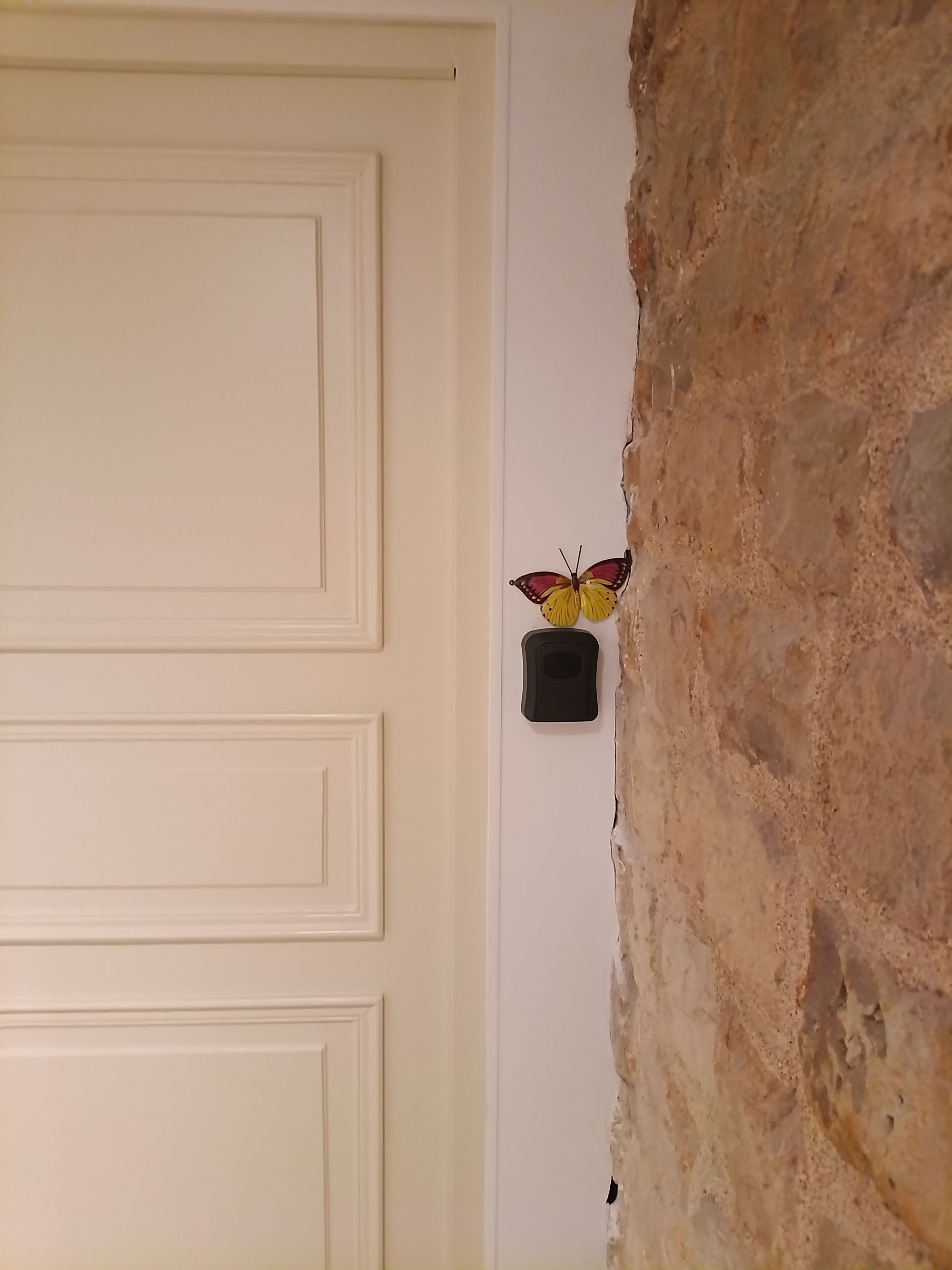 Een witte deur met een vlinderdecoratie op de muur ernaast.