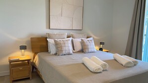 A neatly made bed with a white duvet, two rolled towels, and several pillows. There is a bedside table with a lamp and a remote control. - Luxury 8-person villa on the Côte d'Azur with a pool and ocean views from every room (Fréjus)