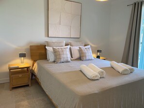 A neatly made bed with a white duvet, two rolled towels, and several pillows. There is a bedside table with a lamp and a remote control. - Luxury 8-person villa on the Côte d'Azur with a pool and ocean views from every room (Fréjus)