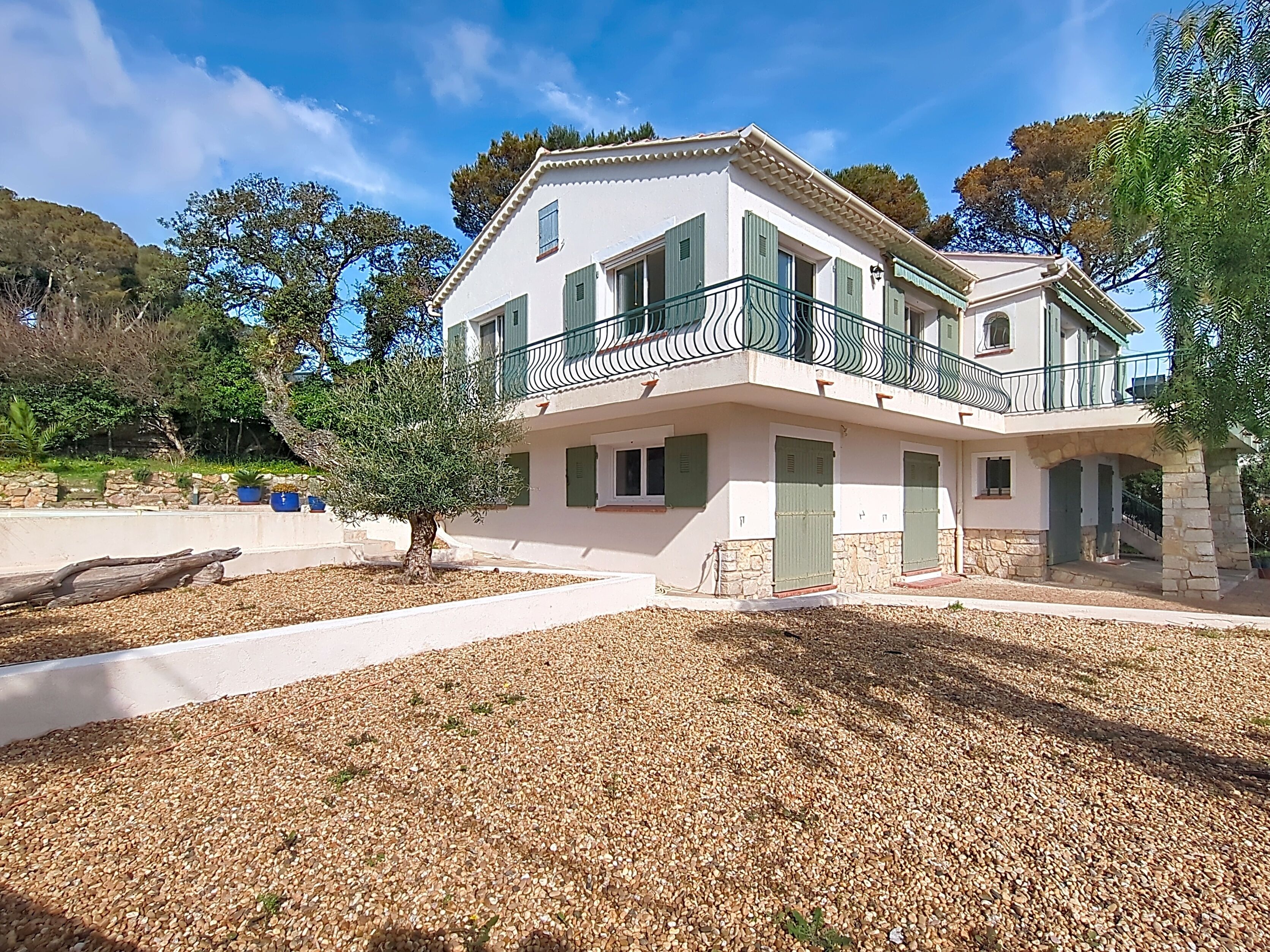 A two-story building with a balcony, stone foundation, and a gravel driveway.