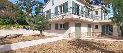 A two-story building with a balcony, stone foundation, and a gravel driveway.