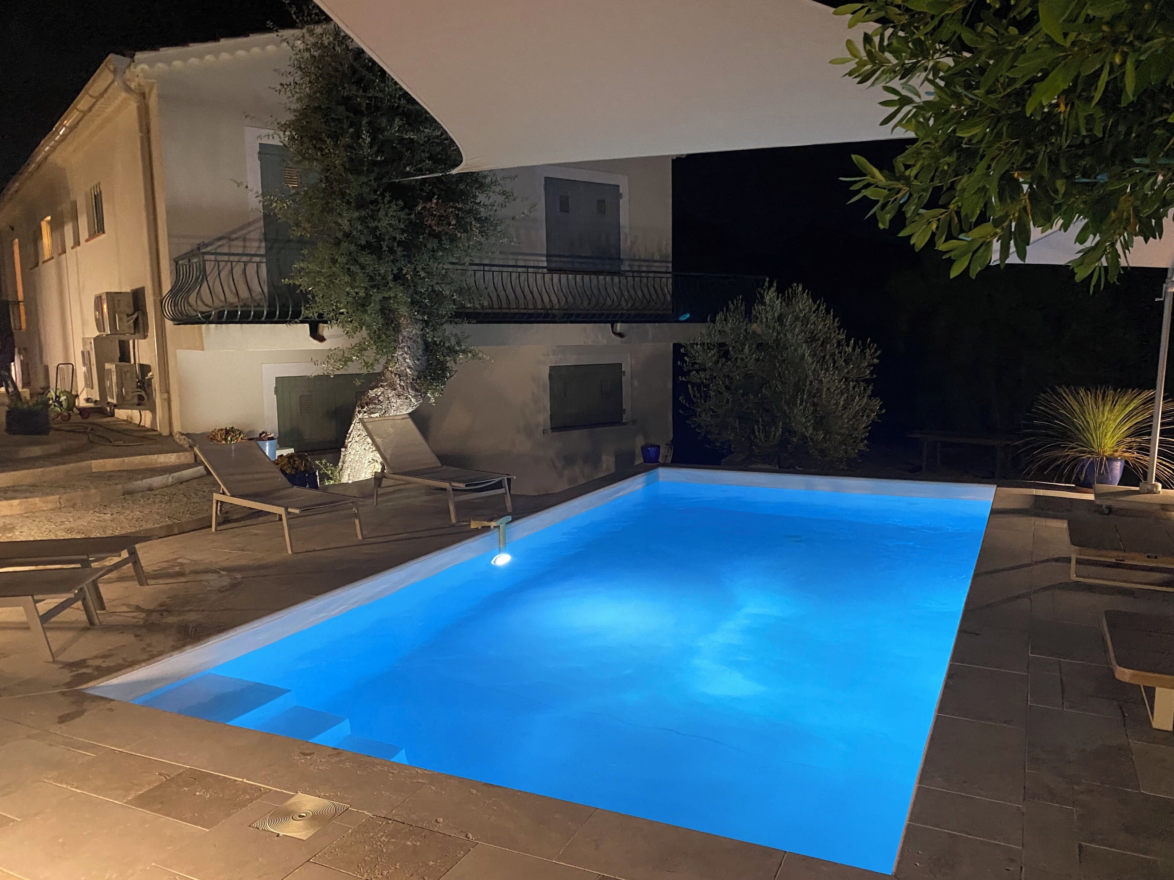 A swimming pool with a clear blue water surface, surrounded by a paved deck with lounge chairs.