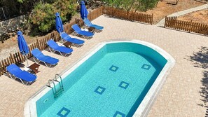 Ein rechteckiger Swimmingpool mit gefliestem Sonnendeck, umgeben von Liegestühlen und Sonnenschirmen.