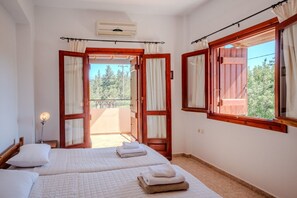 A room with two beds, an air conditioning unit, a nightstand, and a window with curtains. - Villa Oleander- with Private pool & Near the beach (Chania)