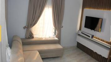 A modern living room with a sofa, a flat-screen TV mounted on the wall, and a window with curtains.