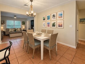 A dining area with a white table, wicker chairs, and a chandelier. - 5-bedroom beach house with pool - 2 blocks from beach, 1 hr from Disney (Satellite Beach)