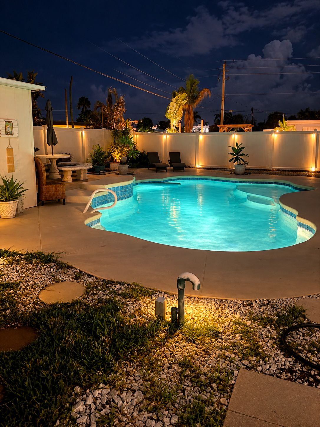 A swimming pool with a curved edge, surrounded by a white fence, and equipped with a water feature.