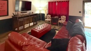Ein Wohnzimmer mit einem roten Ledersofa, einem Flachbildfernseher, einem kleinen Tisch und einem roten Vorhang.