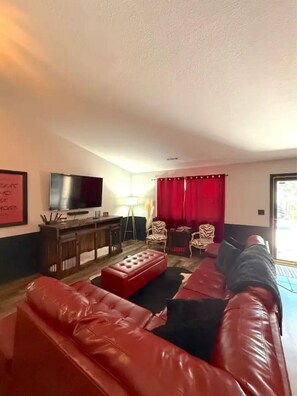 Ein Wohnzimmer mit einem roten Ledersofa, einem Flachbildfernseher, einem kleinen Tisch und einem roten Vorhang.