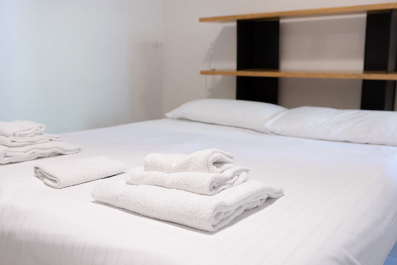 A neatly made bed with white linens and a stack of folded towels.