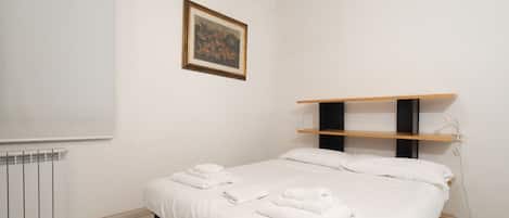 A bedroom with a bed, a radiator, a shelf, and a framed picture on the wall.