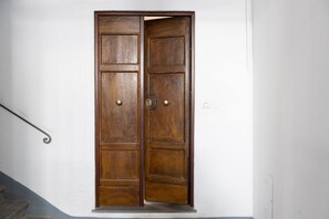A wooden double door with a metal handle and a keyhole, set in a white wall with a metal stair railing to the left. - San Zanobi Central Stay (Florence)