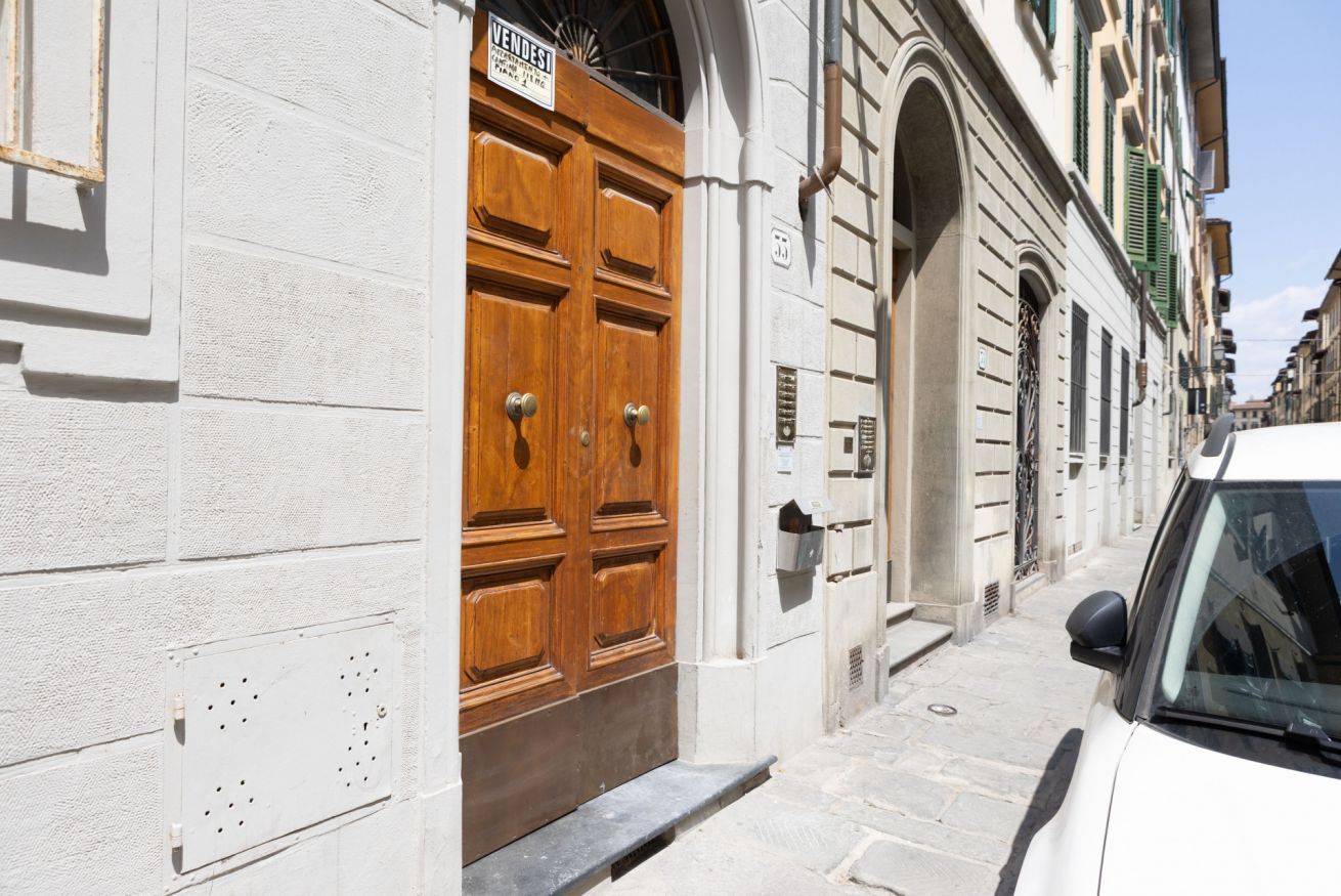 Una calle estrecha con un edificio blanco que tiene una puerta de madera grande y un letrero encima.