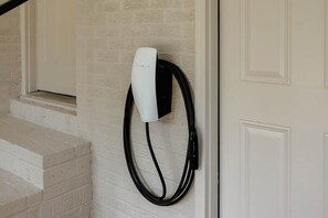 A Tesla charging station mounted on a white brick wall next to a white door.