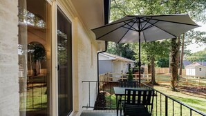 A balcony with a table and chairs, a large umbrella, and a view of a residential area with houses and trees. - Just off S. Milledge 3BD/2BA Pet Friendly with EV Charger (Athens)