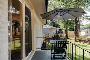 Een balkon met een tafel en stoelen, een grote parasol en uitzicht op een woonwijk met huizen en bomen.