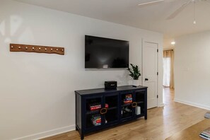 Una sala de estar moderna con un televisor de pantalla plana montado en la pared, una consola de madera oscura con puertas de cristal y un pasillo que conduce a otra habitación.