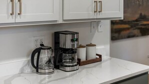 A kitchen with white cabinets, a coffee maker, a glass carafe, and a coffee pot on a marble countertop. - Just off S. Milledge 3BD/2BA Pet Friendly with EV Charger (Athens)