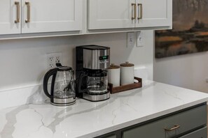 Een keuken met witte kasten, een koffiezetapparaat, een glazen kan en een koffiepot op een marmeren aanrecht.