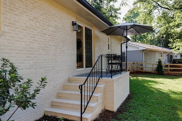 A house with a brick exterior, a front porch with steps, a black railing, and a wooden fence.