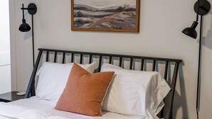 A bed with white bedding and a single brown pillow, a black headboard, and a painting of a landscape on the wall. - Just off S. Milledge 3BD/2BA Pet Friendly with EV Charger (Athens)