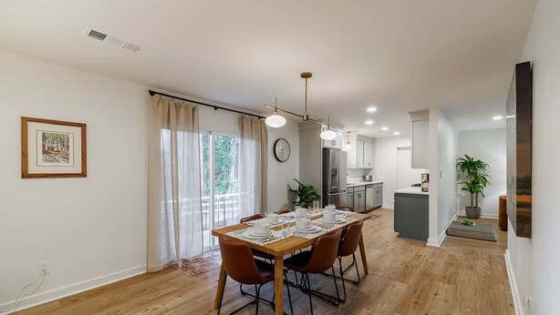 A dining area with a wooden table set for four, a kitchen in the background, and a living area with a sofa and a plant. - Just off S. Milledge 3BD/2BA Pet Friendly with EV Charger (Athens)