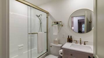 Une salle de bain moderne avec une douche à parois de verre, des toilettes, un lavabo avec un miroir et un meuble-lavabo avec espace de rangement.