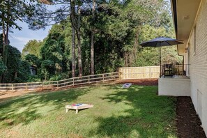 Un patio trasero cercado con una terraza de madera, una mesa de picnic y una sombrilla grande.