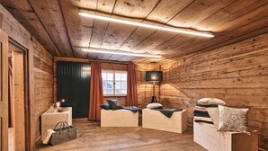 L’intérieur d’une cabane en rondins, avec des murs en bois, une cheminée, deux canapés blancs, une lampe sur pied et une fenêtre avec des rideaux.