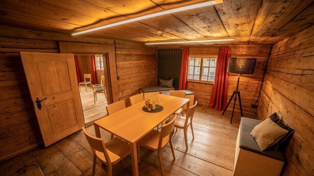 L’intérieur d’un chalet en bois comprend une table à manger, des chaises, un canapé et une fenêtre avec des rideaux.