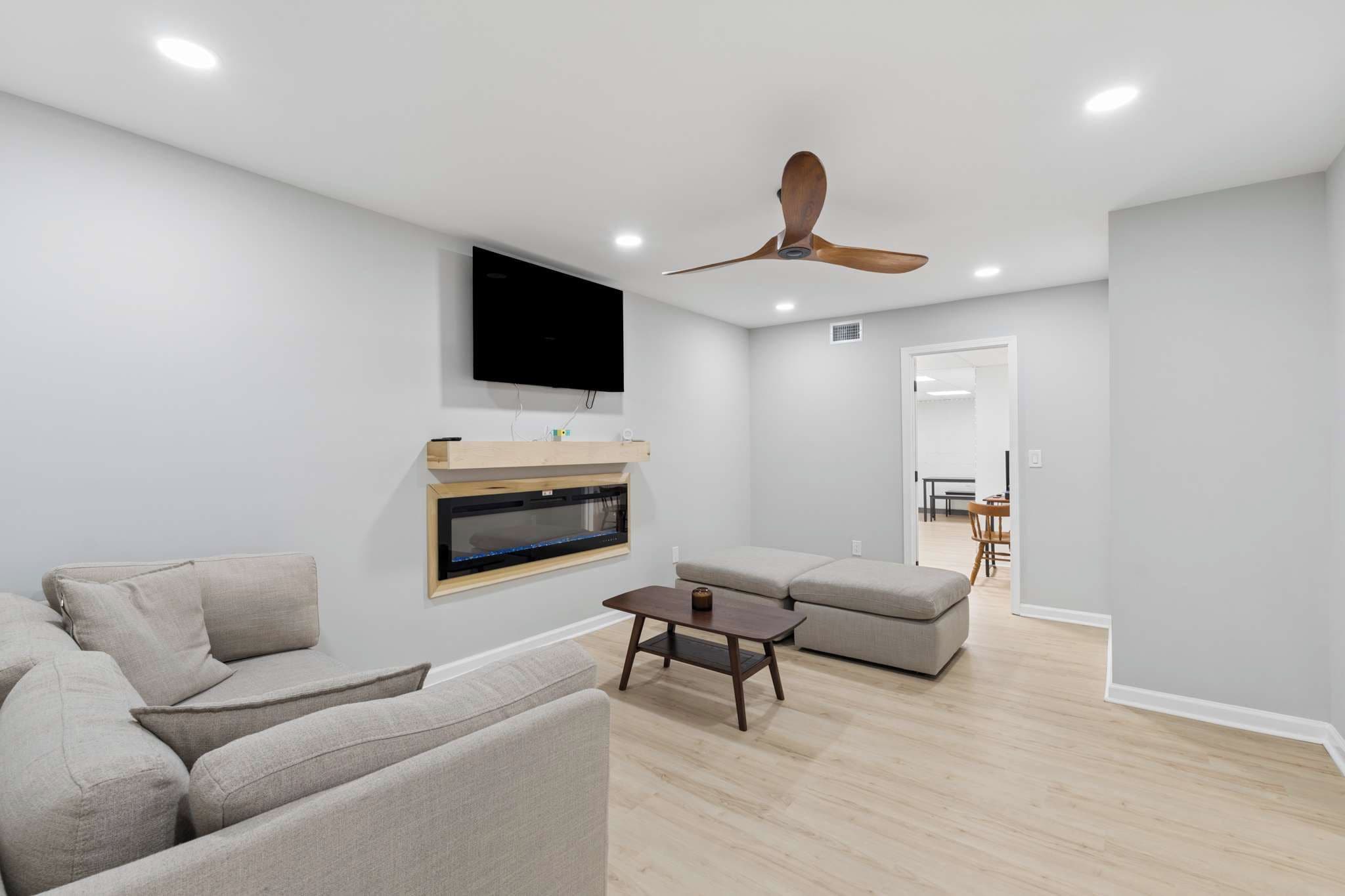 A modern living room with a flat-screen TV, a ceiling fan, and a wooden coffee table.
