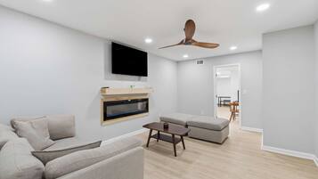 A modern living room with a flat-screen TV, a ceiling fan, and a wooden coffee table.