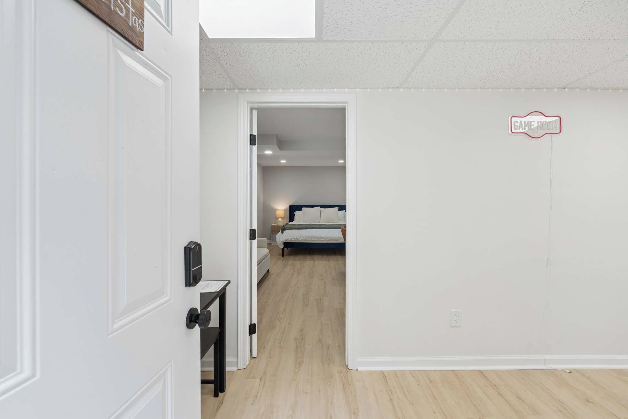 Un couloir mène à une chambre à coucher qui contient un lit, une table de chevet et une commode. Une porte se trouve sur le côté gauche, avec une serrure et une poignée.