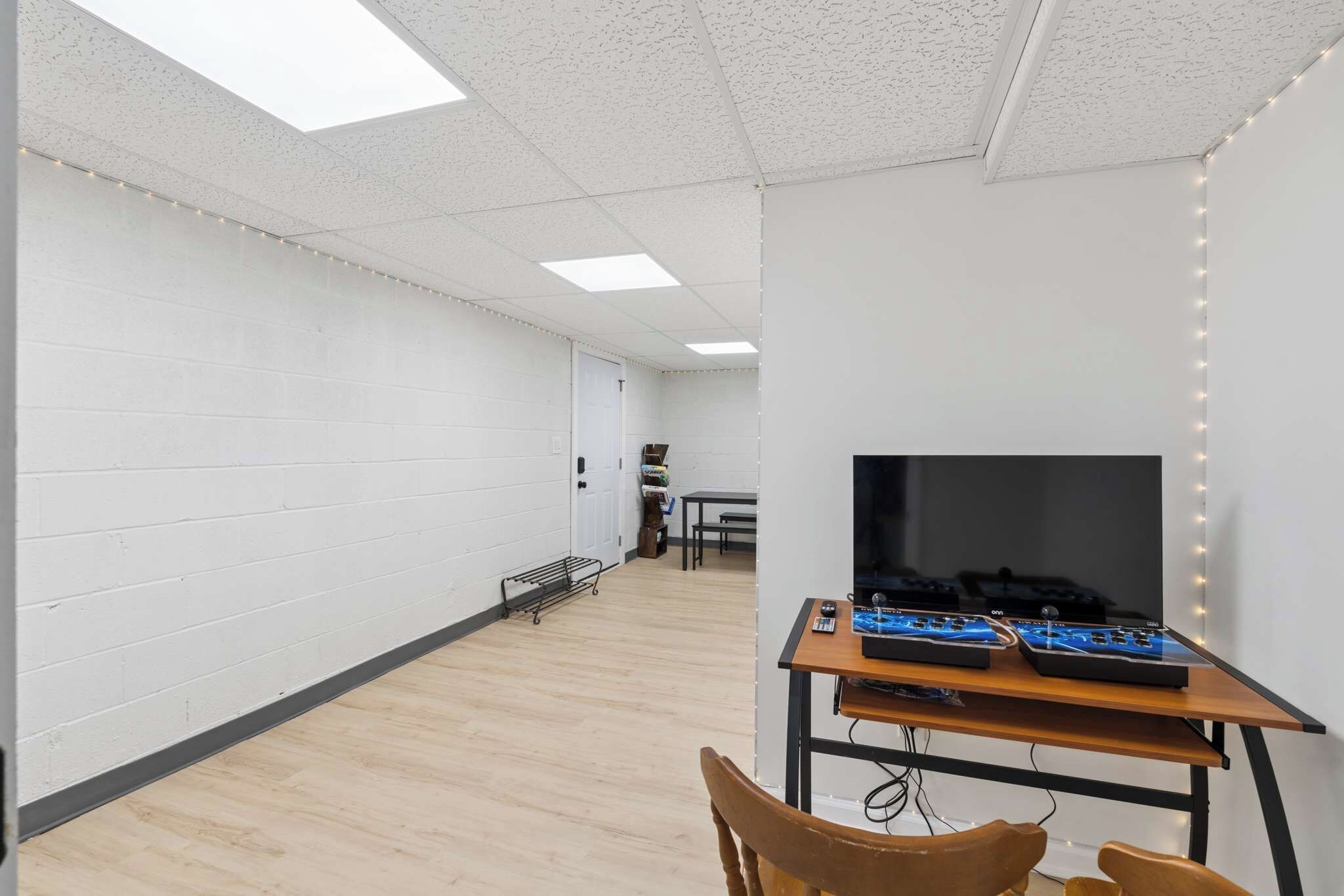 A room with white walls, a wooden floor, a desk with electronic equipment, and a television.