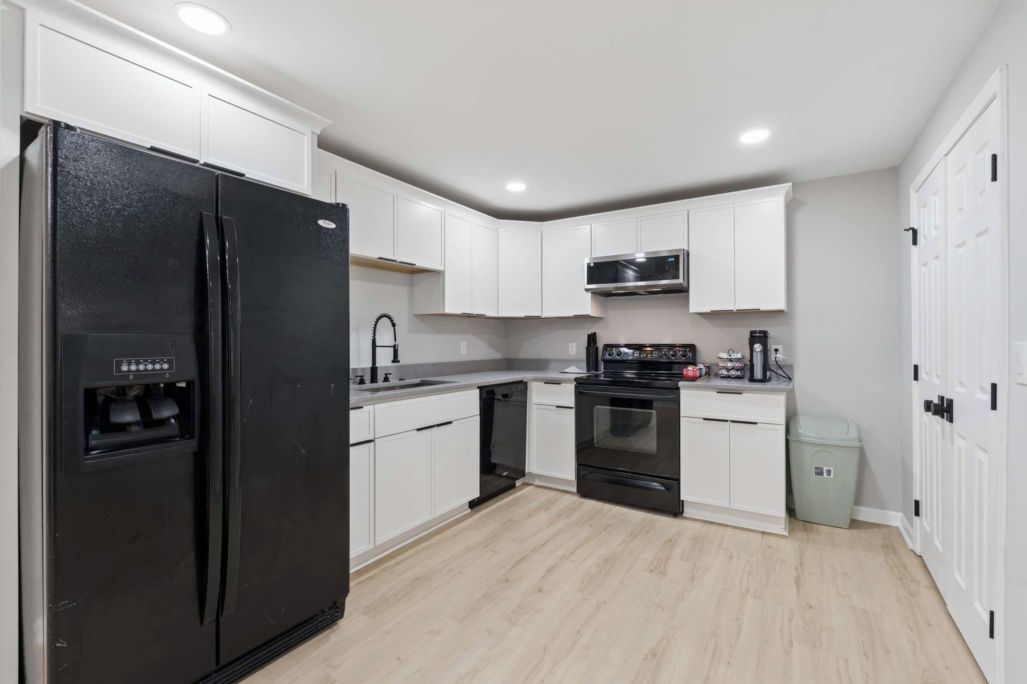 A modern kitchen with white cabinetry, a black refrigerator, a microwave, an oven, and a dishwasher.