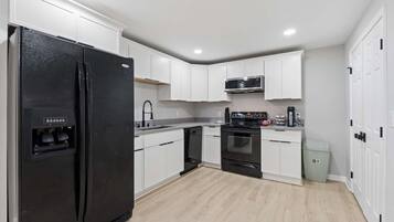 A modern kitchen with white cabinetry, a black refrigerator, a microwave, an oven, and a dishwasher.
