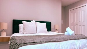 A neatly made bed with white bedding and pillows, a green headboard, and a rolled towel on the side.