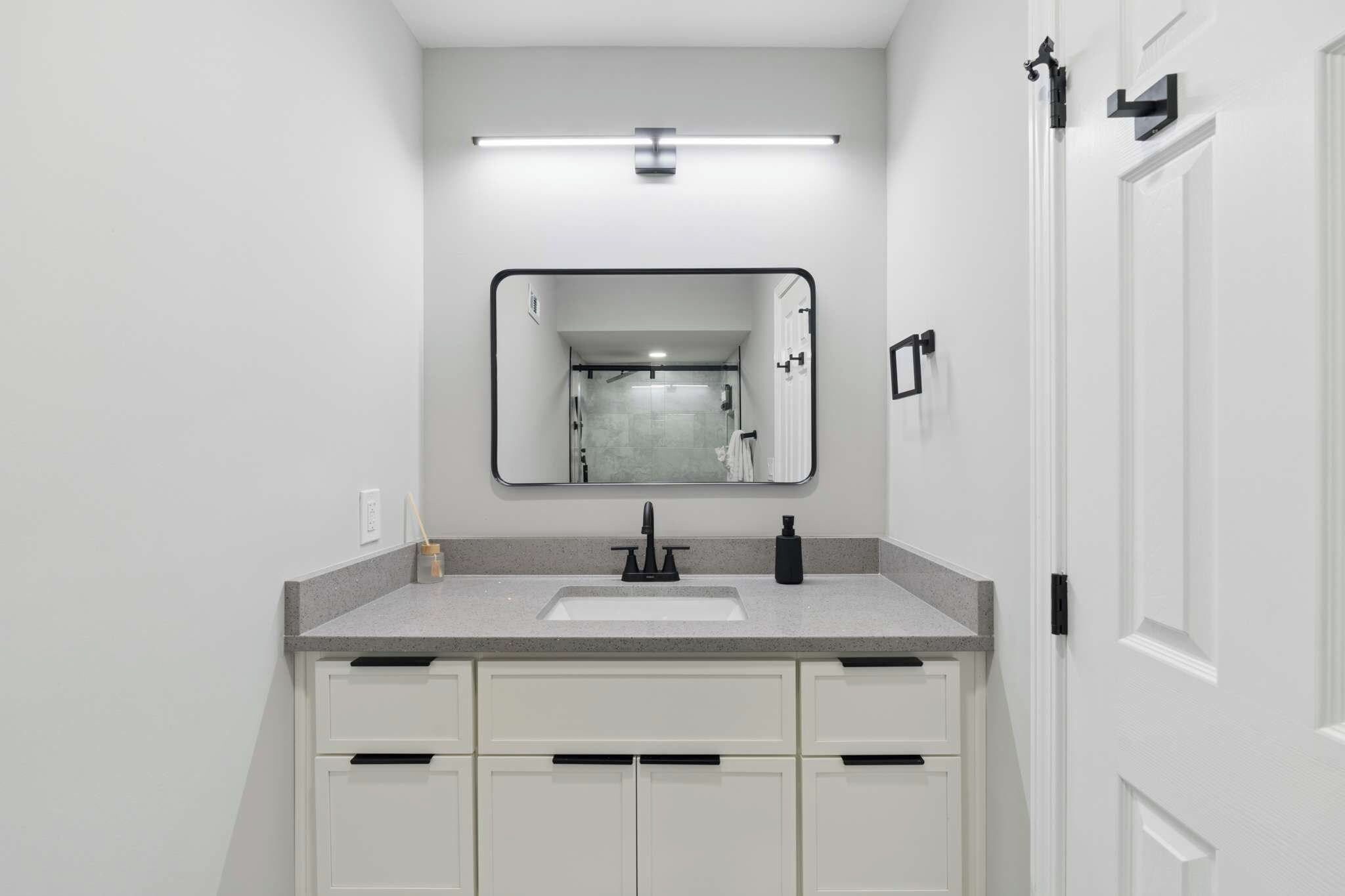 A modern bathroom with a white vanity, a large mirror, and a shower visible in the reflection.
