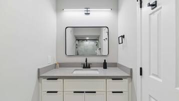A modern bathroom with a white vanity, a large mirror, and a shower visible in the reflection.