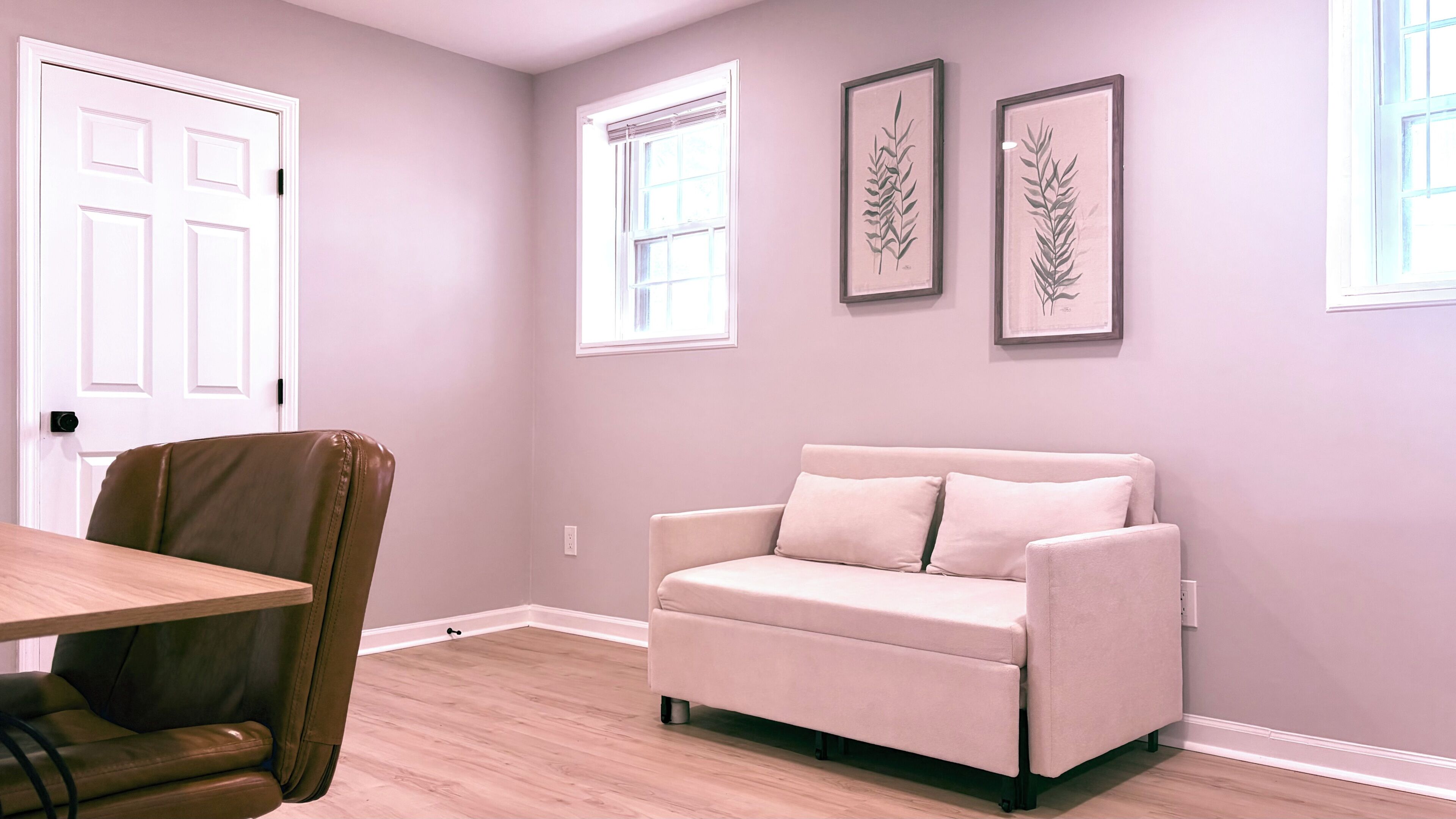A room with a beige sofa, a wooden table, and two framed botanical prints on the wall.