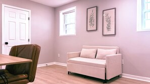 Um quarto com um sofá bege, uma mesa de madeira e duas gravuras botânicas emolduradas na parede.