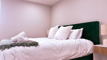 Uma cama bem arrumada com roupa de cama e almofadas brancas, cabeceira verde e mesa de cabeceira com abajur.