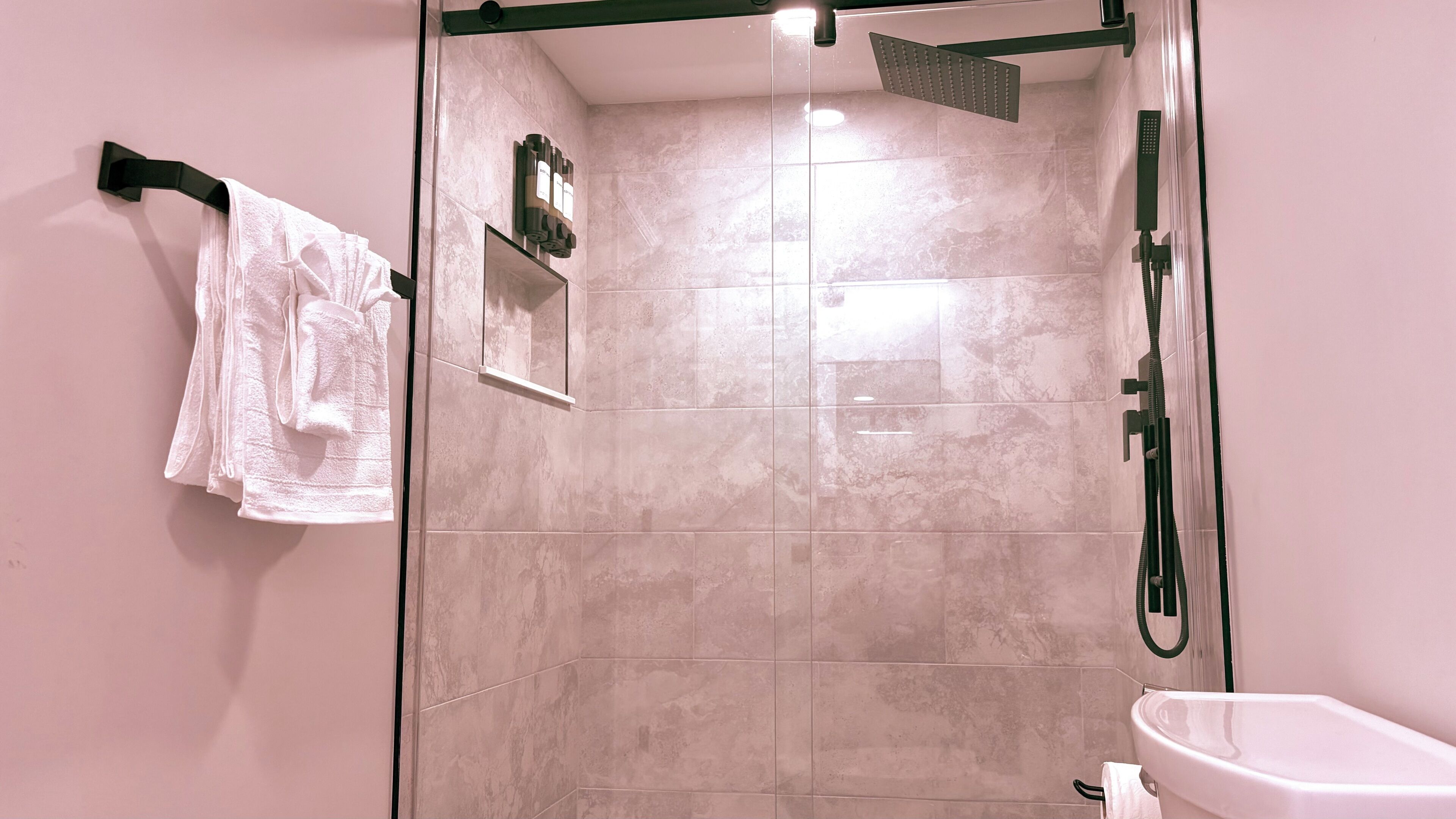 A modern bathroom with a glass-enclosed shower, a toilet, and a towel rack with multiple towels.