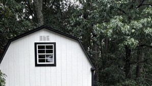 A white building with a black door and window, surrounded by trees.